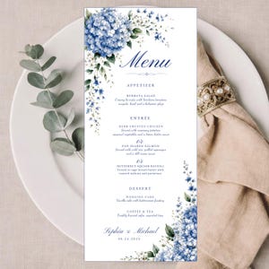 May include: A vertical rectangular menu card featuring a watercolor illustration of blue hydrangea flowers and green foliage. The text reads Menu, Appetizer, Entree, Dessert, and lists food items for Sophia & Michael on 08.24.2025 in dark blue font.