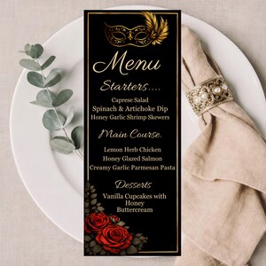 May include: A black menu card with gold trim, featuring a gold masquerade mask and feather design. The menu lists starters, main courses, and desserts, including Caprese salad and honey glazed salmon. Red roses adorn the bottom.