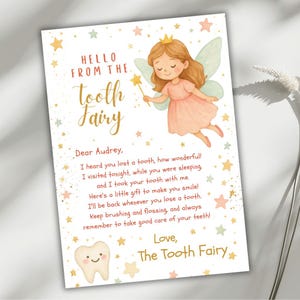 May include: A charming Tooth Fairy letter, with a cartoon fairy in a pink dress, holding a wand and wearing wings. The card has gold text that reads "Hello from the Tooth Fairy" and a personalized message. The card is decorated with stars.