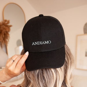 Pu&ograve; includere: Un cappello da baseball nero con la parola "ANDIAMO" ricamata in bianco sul davanti.