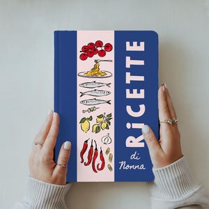 May include: A blue cookbook featuring the word "RICETTE" in white, and illustrations of Italian cuisine. The cookbook has a pink central stripe with drawings of tomatoes, pasta, fish, lemons, garlic, and chillies. The words "di Nonna" are at the bottom.
