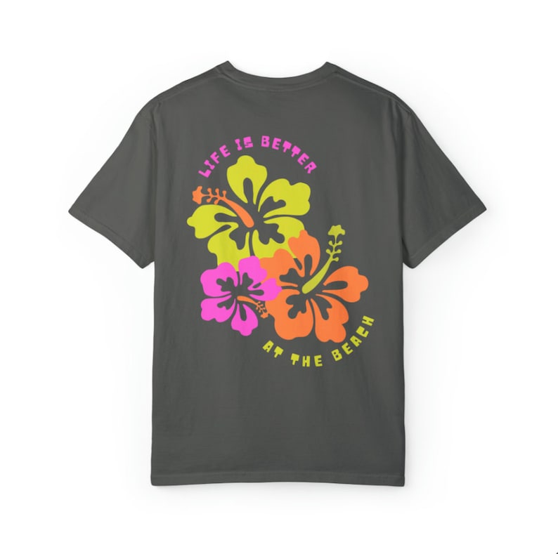 May include: Dark gray t-shirt featuring a colorful floral design with the text "LIFE IS BETTER AT THE BEACH." The graphic includes yellow, orange, and pink hibiscus flowers. The shirt is a casual, short-sleeved style.