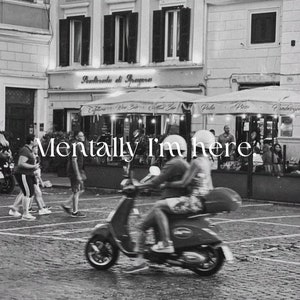Pu&ograve; includere: Una foto in bianco e nero di una coppia su uno scooter rosso davanti a un bar a Roma, Italia. Il testo "Mentally I'm here." &egrave; sovrapposto all'immagine.