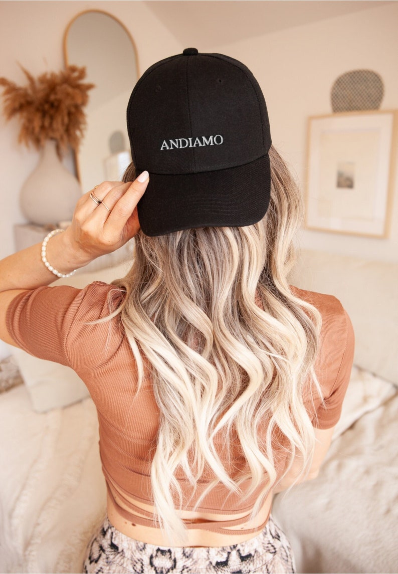 Pu&ograve; includere: Un cappello da baseball nero con la parola "ANDIAMO" ricamata in bianco sul davanti.