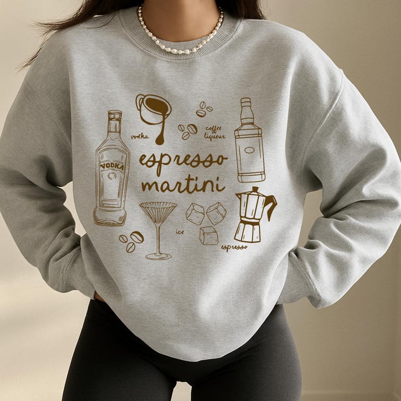 K&ouml;nnte beinhalten: Hellgraues Sweatshirt mit braunem Grafikdesign. Das Design zeigt die Worte "Espresso Martini" und Illustrationen von Cocktailzutaten wie Wodka, Kaffeelik&ouml;r, Espresso, Eis und einem Martiniglas.