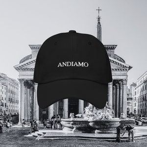 Pu&ograve; includere: Cappellino da baseball nero con il testo "ANDIAMO" ricamato in bianco davanti a un edificio storico a Roma, Italia.