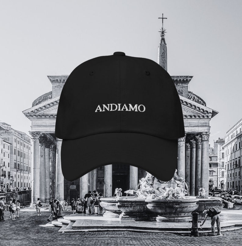 Pu&ograve; includere: Cappellino da baseball nero con il testo "ANDIAMO" ricamato in bianco davanti a un edificio storico a Roma, Italia.