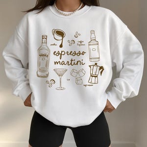 K&ouml;nnte beinhalten: Wei&szlig;es Sweatshirt mit braunem Grafikdesign. Das Design zeigt die Worte "Espresso Martini" und Illustrationen von Wodka, Kaffeelik&ouml;r, Espresso, Eis und einem Martiniglas. Das Design ist zentriert.