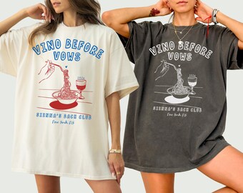 以下が含まれることがあります： クリーム色とチャコール色の2枚のオーバーサイズTシャツ。グラフィックデザインが施されており、「VINO BEFORE VOWS」の文字とスパゲッティとワイングラスのイラストが描かれています。下部には「SIENNA'S BACH CLUB New York, NY」と書かれています。