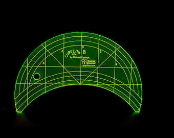 Puede incluir: Regla de acolchado Curve It 8 echo de plástico verde con marcas para 0, 2, 4 y 8 pulgadas. La regla tiene forma de semicírculo y tiene un agujero en el centro.