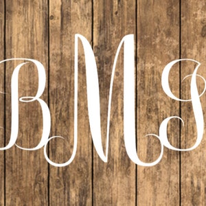 May include: White monogram letters "BMS" in a cursive font on a brown wood background.