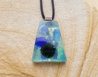 May include: A teal, blue, and green glass pendant with a black circle and gold flecks. The pendant is hanging from a black cord.
