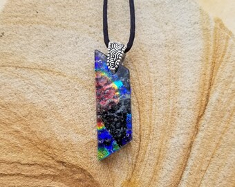 May include: A black cord necklace with a silver pendant featuring a multi-colored glass piece with iridescent blue, green, and red hues. The glass piece is shaped like a long, thin rectangle with a slightly pointed top.