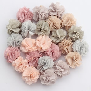 Op de afbeelding: Een verzameling van 20 kleine, stoffen bloemenversieringen in tinten roze, grijs en beige. De bloemen zijn gemaakt van zacht, gerimpeld stof en hebben een delicate, vrouwelijke uitstraling.