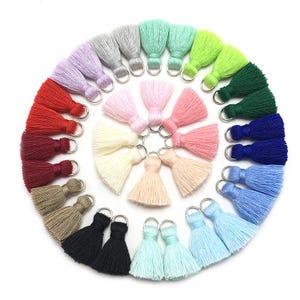 May include: Assortment of 20 colorful tassel trims with silver rings. The tassels are made of soft yarn and come in a variety of colors, including red, blue, green, pink, and white.