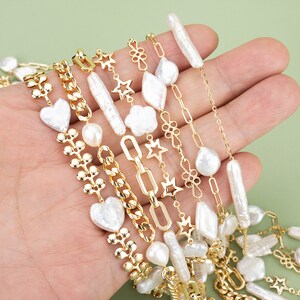 May include: A collection of gold chain necklaces with pearl and shell charms. The chains feature different styles, including a chunky curb chain, a delicate cable chain, and a chain with small flower charms. The charms include a heart, a star, and a flower.