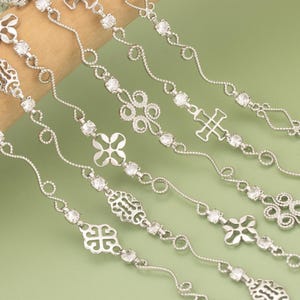 Könnte beinhalten: Nahaufnahme mehrerer silberfarbener Armbänder mit verschiedenen dekorativen Designs. Jedes Armband verfügt über klare, funkelnde Edelsteine und komplizierte Muster, darunter Blumen-, Kreuz- und geometrische Formen. Die Armbänder werden vor einem grünen Hintergrund präsentiert.