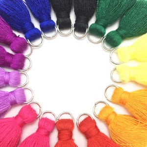May include: A circle of colorful yarn tassels with silver rings. The tassels are arranged in a rainbow pattern, starting with purple and ending with yellow.
