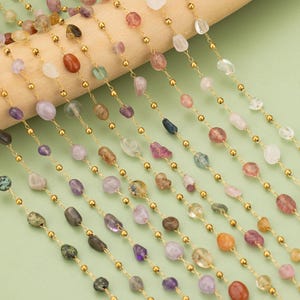 May include: A selection of gemstone beads strung on gold chains. The beads are of various shapes and sizes, and include amethyst, rose quartz, aquamarine, and other semi-precious stones.