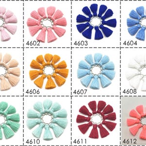 May include: Twelve sets of ten small, colorful tassels with metal rings. Each set is arranged in a circle on a white background. The colors include pink, peach, orange, blue, light blue, white, green, light green, burgundy, and coral.