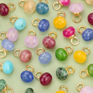 May include: Assortment of colourful gemstone charms with gold accents. The charms are in various shapes and sizes, including round, oval, and teardrop.