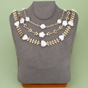 May include: A layered necklace with gold chain links and white pearl-like beads in heart and star shapes.
