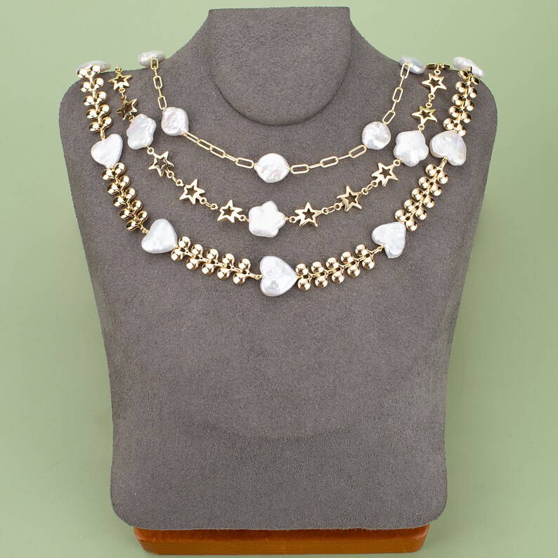 May include: A layered necklace with gold chain links and white pearl-like beads in heart and star shapes.