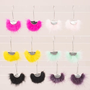 May include: A collection of colorful, fluffy earrings. Each earring features a silver-toned metal base with a fan-shaped design of vibrant fur. Colors include hot pink, white, yellow, mint green, black, and purple. The earrings are displayed on a clear, grid-like background.