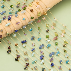 May include: A collection of gold chains with various coloured gemstone chips. The chains are laid out on a wooden surface.