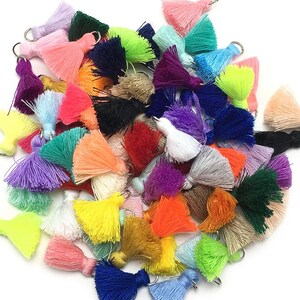 May include: A large assortment of colorful tassels with metal rings. The tassels are made of soft yarn and come in a variety of colors, including pink, blue, green, yellow, orange, red, purple, and white.
