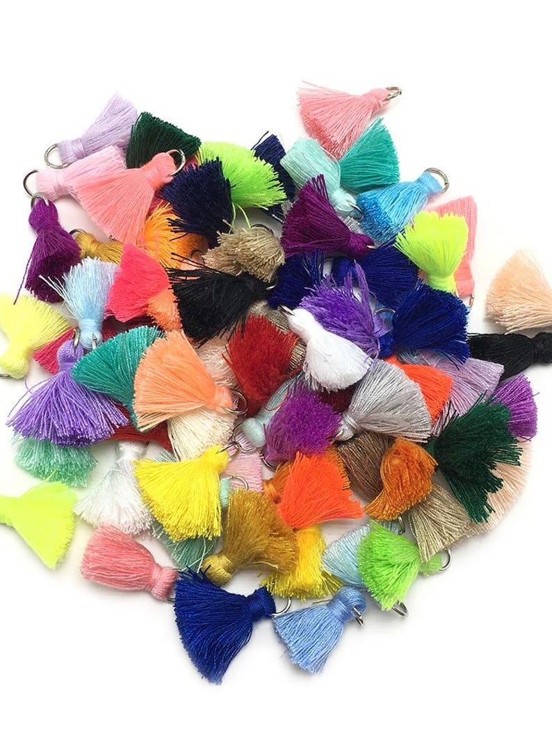 May include: A large assortment of colorful tassels with metal rings. The tassels are made of soft yarn and come in a variety of colors, including pink, blue, green, yellow, orange, red, purple, and white.