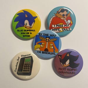 Op de afbeelding: Een verzameling van vijf ronde buttonspins. De buttons tonen stripfiguren en zinnen, waaronder Sonic the Hedgehog, Dr. Eggman en Shadow. De buttons zijn in verschillende kleuren, waaronder blauw, geel en paars.