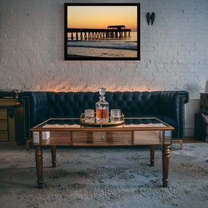 Puede incluir: Un sal&oacute;n con un cuadro enmarcado de un paisaje de puesta de sol. Un sof&aacute; de cuero azul oscuro, una mesa de centro de madera con tapa de espejo y un juego de decantador est&aacute;n en primer plano. La habitaci&oacute;n tiene una alfombra y una pared de ladrillo blanco.