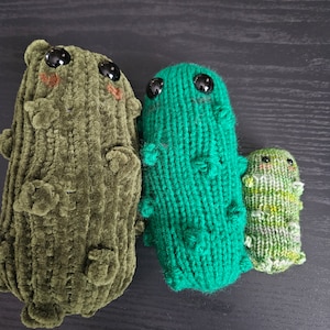 Könnte beinhalten: Drei gestrickte Plüschtiere in Form von Gurken. Die erste ist dunkelgrün, die zweite ist hellgrün und die dritte ist hellgrün mit einem melierten Muster.