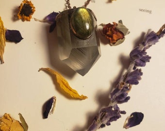 May include: A silver and clear crystal point pendant with a green labradorite gemstone set in a copper frame. The pendant is hanging from a copper chain.