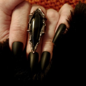 May include: A black onyx ring with a pointed, jagged design. The ring is set in a copper-toned metal and has a dark, almost black, finish.
