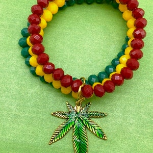 May include: A red, yellow, and green beaded bracelet with a gold marijuana leaf charm.