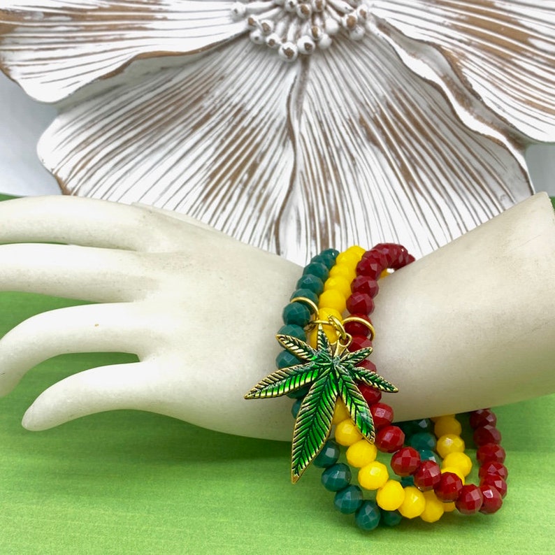 May include: Three layered beaded bracelets in red, yellow, and green with a green and gold marijuana leaf charm.