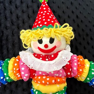 Puede incluir: Mu&ntilde;eca de payaso hecha a mano con sombrero de lunares rojos y blancos y cuello con volantes. La mu&ntilde;eca tiene pelo de hilo amarillo, una cara sonriente y un cuerpo colorido con secciones de lunares de colores del arco&iacute;ris.