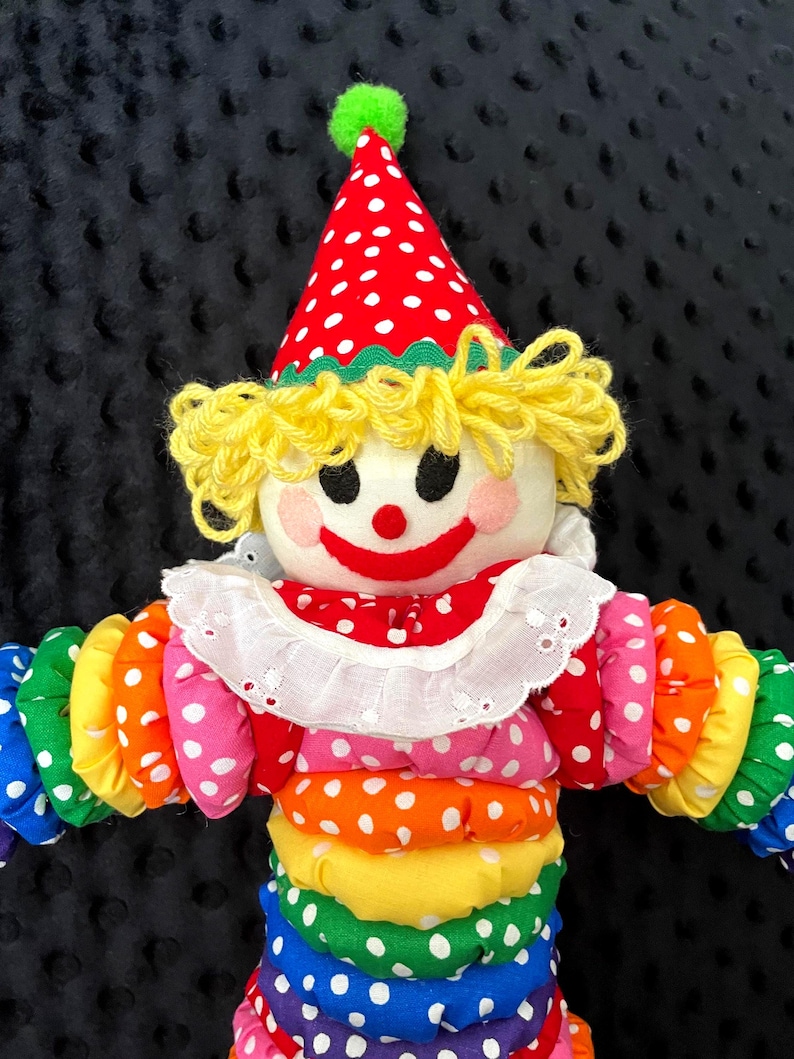 Puede incluir: Mu&ntilde;eca de payaso hecha a mano con sombrero de lunares rojos y blancos y cuello con volantes. La mu&ntilde;eca tiene pelo de hilo amarillo, una cara sonriente y un cuerpo colorido con secciones de lunares de colores del arco&iacute;ris.