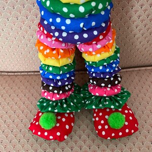 Puede incluir: Piernas de mu&ntilde;eco payaso coloridas. Las piernas est&aacute;n hechas de tela en capas en colores del arco&iacute;ris, cada capa con lunares blancos. Los pies son rojos con lunares blancos y pompones verdes.