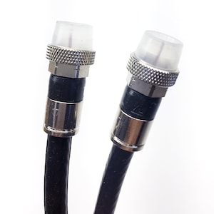 May include: Two black coaxial cables with silver F-type connectors and white plastic caps. The connectors have a silver ring around the base.