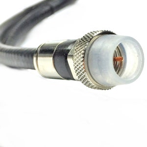 May include: A close-up of a black coaxial cable with a silver F-type connector. The connector has a clear plastic cover over the center pin.