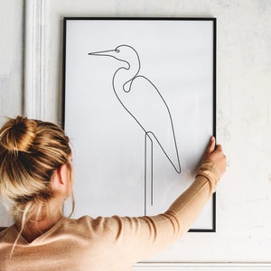 May include: A black framed print with a line drawing of a white egret standing on one leg. The egret is facing the left side of the image.
