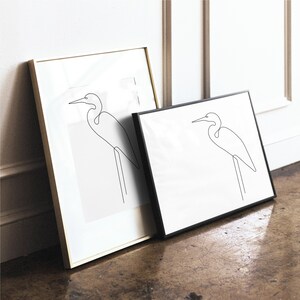 May include: Two framed line drawings of a white egret bird in a minimalist style. The frames are gold and black.