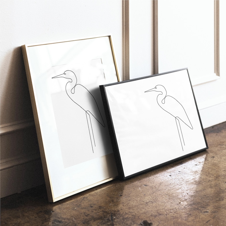 May include: Two framed line drawings of a white egret bird in a minimalist style. The frames are gold and black.