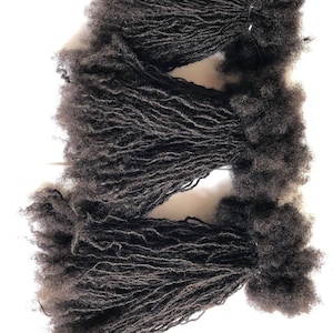 Puede incluir: Tres paquetes de rastas de cabello humano negro. Las rastas son largas y gruesas, y están dispuestas en un estilo suelto y fluido.