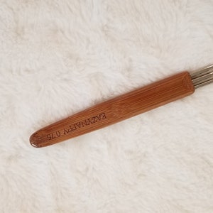 May include: A wooden tool with a handle and five metal needles. The handle is engraved with the text "EZ KNITTER 0.75".