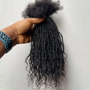 May include: A bundle of black, curly hair extensions. The hair is held together at the top, with the individual strands cascading downwards. The texture appears natural, with varying curl patterns and a dark, rich color. The extensions are designed for styling.