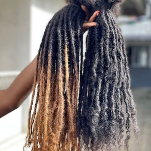 Op de afbeelding: Twee sets lange dreadlocks, één set is donkerbruin en de andere is een lichtbruine ombre. De dreadlocks hangen naar beneden en zijn licht gekruld aan de uiteinden.